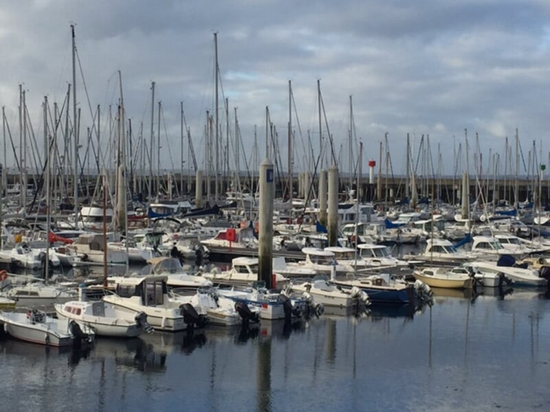 Port de plaisance rempli de nombreux bateaux à moteur et voiliers amarrés sous un ciel nuageux.