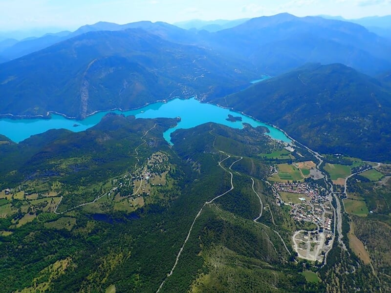 Vue aérienne d'un lac turquoise entouré de collines verdoyantes et de petites routes sinueuses.