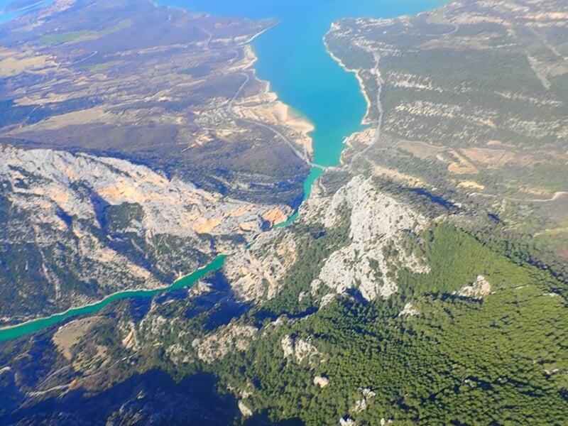Paysage vu du ciel montrant un lac étroit entouré de falaises rocheuses et de forêts denses.