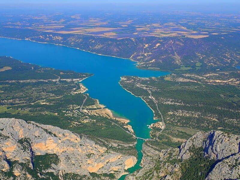 Panorama aérien d'un lac bleu profond avec des montagnes rocheuses et des zones boisées autour.