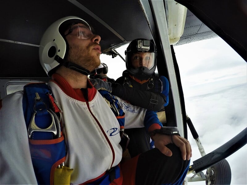 Deux parachutistes en combinaison blanche et noire regardent vers l'extérieur d'un avion avant de sauter.