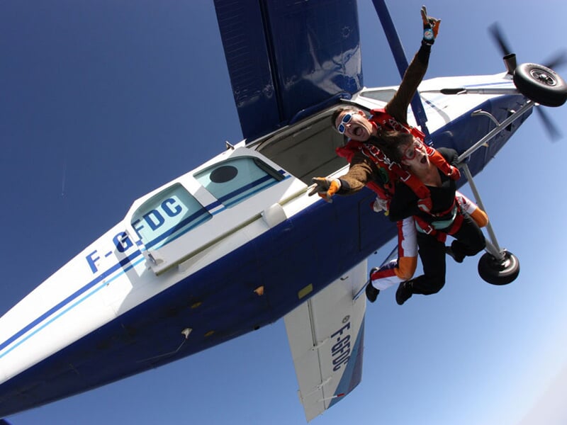 Saut en parachute extrême avec un instructeur vêtu d'un costume original. Accrochés en tandem, ils quittent l'avion en pleine vitesse, l'instructeur levant le bras en signe d'excitation tandis que son