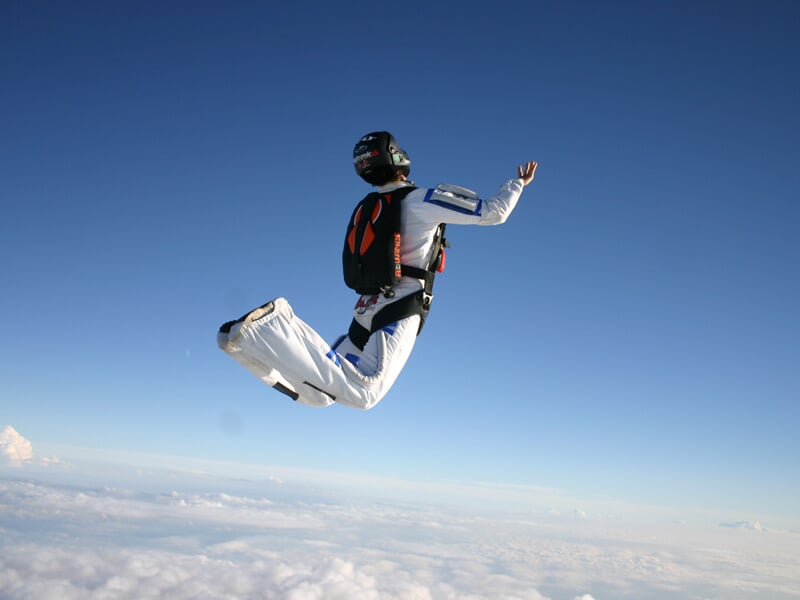 Un parachutiste en combinaison blanche et noire en position de chute libre avec un ciel bleu clair en arrière-plan.