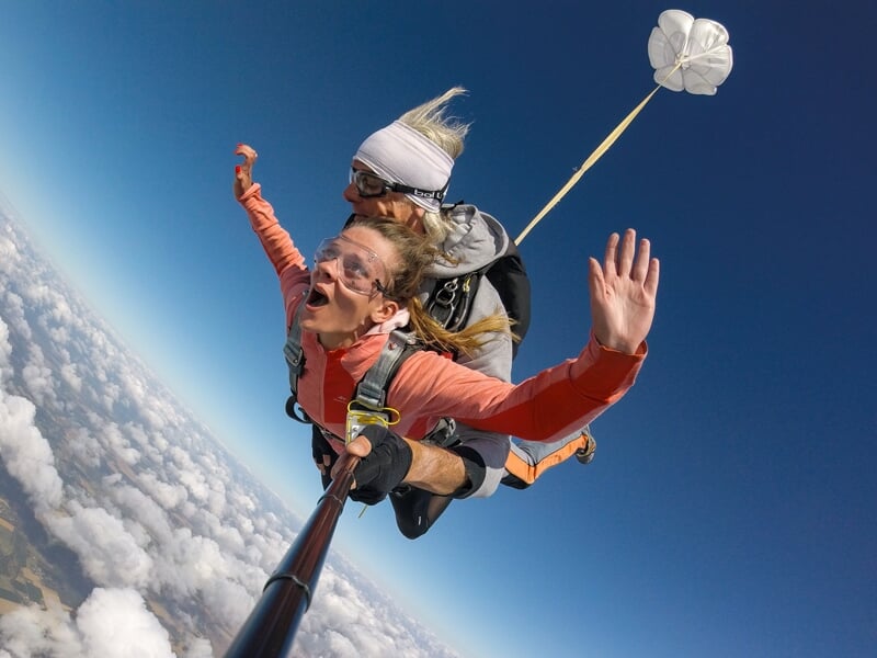 Deux femmes en chute libre en tandem, souriantes, avec un petit parachute de secours blanc déployé.