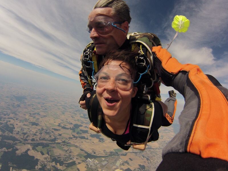 Deux personnes en chute libre lors d'un saut en parachute, avec un paysage de campagne visible en dessous.