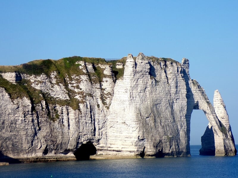 Falaises d'Étretat : Les célèbres falaises de calcaire blanc d'Étretat en Normandie, avec leurs formations rocheuses spectaculaires, se dressent majestueusement au-dessus de l'eau. Le ciel bleu et l'e