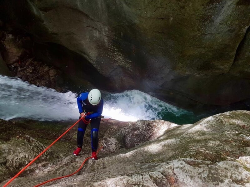 Canyoneur équipé d'un casque et d'un harnais descendant en rappel le long d'une cascade rocheuse.