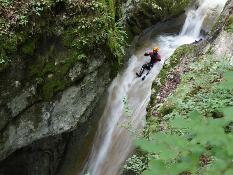 Canyoneur glissant sur un toboggan naturel formé par une cascade dans un environnement verdoyant.