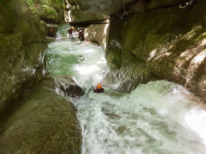 Personne en combinaison et casque orange descendant une rivière agitée dans un canyon étroit et rocheux.