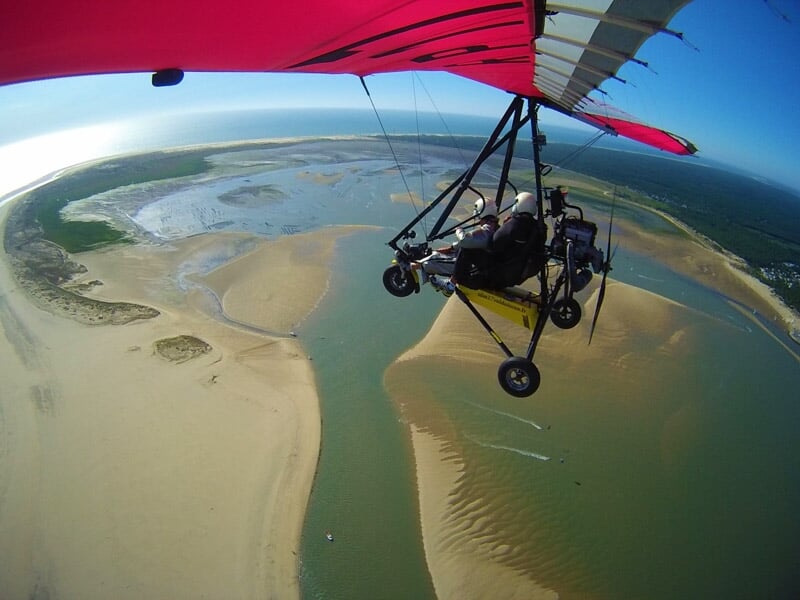 ULM survolant un estuaire avec des bancs de sable et des eaux peu profondes, sous un ciel bleu clair
