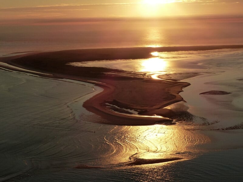 Coucher de soleil sur une île sablonneuse entourée d'eau, avec des reflets dorés sur la mer et le sable