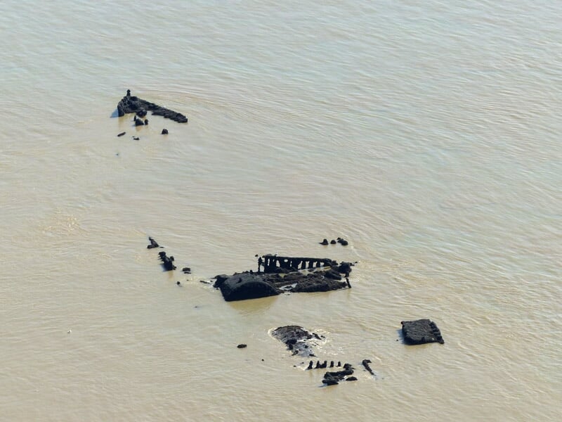 Épave de bateau submergée dans une eau trouble, avec des structures métalliques et boisées émergeant de la surface