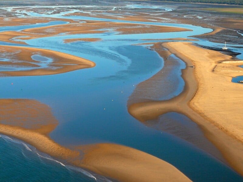 Littoral à marée basse, avec des bancs de sable sinueux et des cours d'eau se jetant dans la mer. Paysage côtier sous une lumière douce