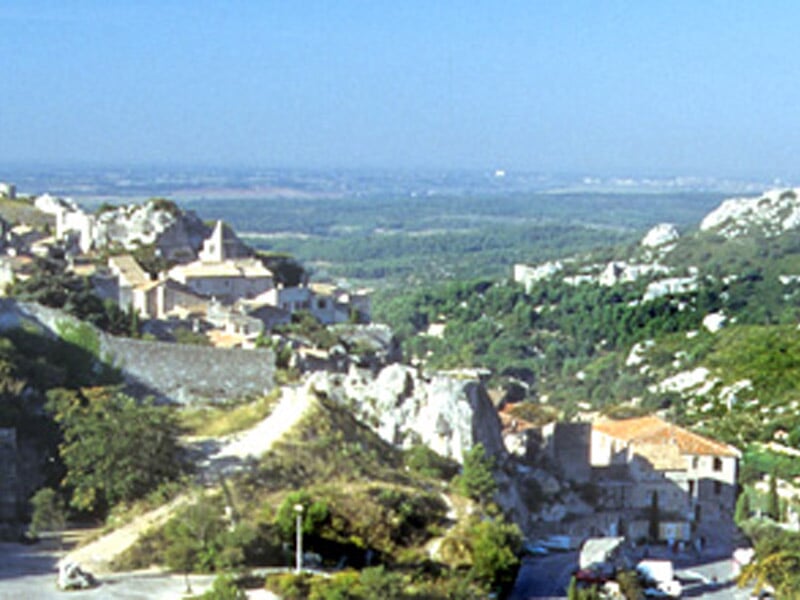 Vue panoramique d'un village perché sur une colline avec des maisons anciennes et une église sous un ciel bleu clair.