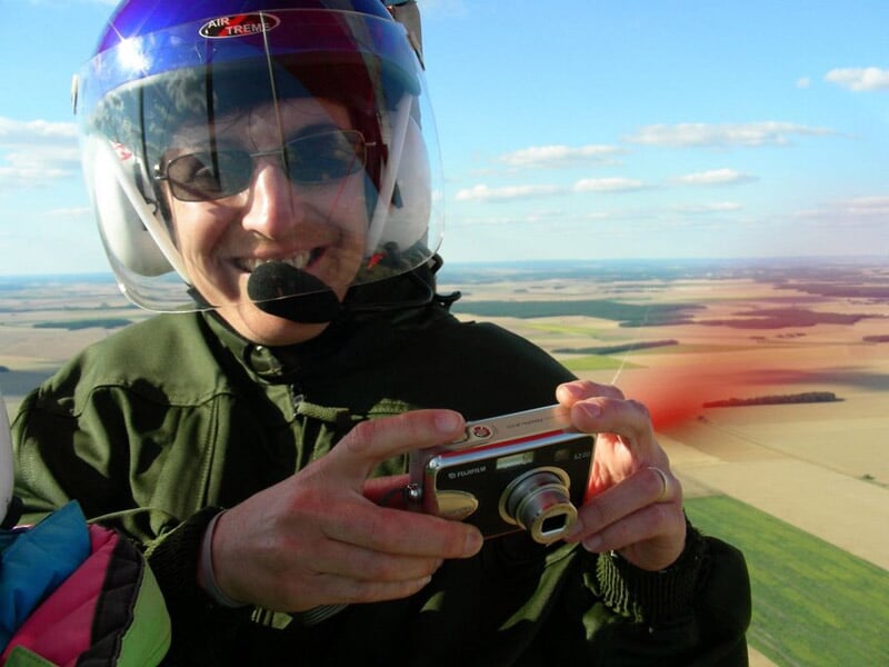 un passager d'avion ULM en plein vol sourit à la caméra en tenant un appareil photo