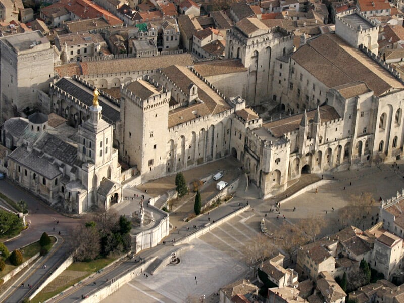 Vue aérienne du Palais des Papes à Avignon, monument historique avec ses tours et remparts, place animée en avant.