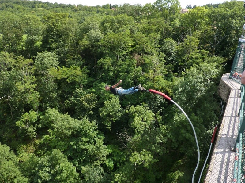 Personne en train de faire un saut à l'élastique depuis un pont au-dessus d'une forêt dense et verte.