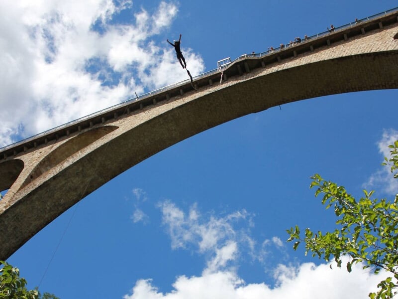 Saut à l'élastique depuis un pont en arc avec ciel bleu et nuages blancs en arrière-plan.
