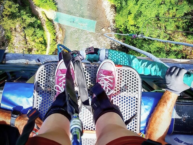 Vue en plongée des pieds d'une personne attachée pour un saut à l'élastique au-dessus d'une rivière.
