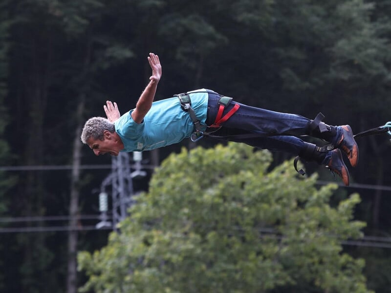 Homme en plein saut à l'élastique, bras écartés, au-dessus d'une forêt dense et feuillue.
