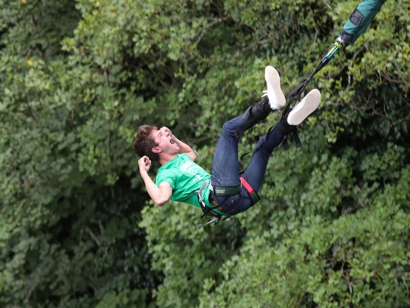 Jeune homme en saut à l'élastique, expression de surprise, suspendu au-dessus des arbres verts.