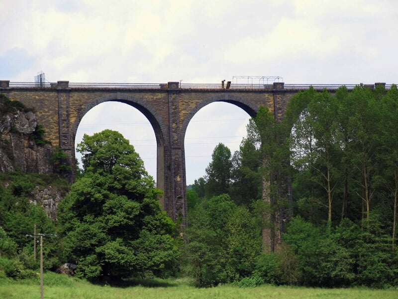 Viaduc en pierre avec deux grandes arches au-dessus d'une prairie verte et d'arbres feuillus.