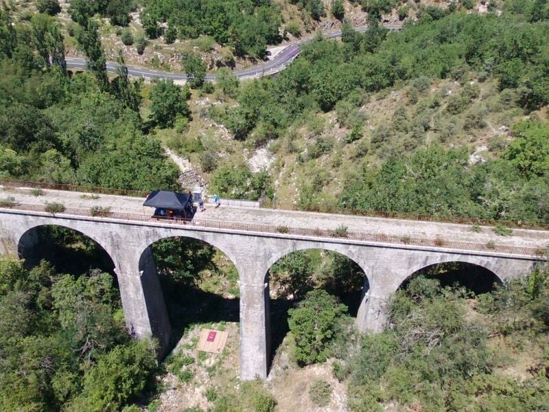 Vue aérienne d'un viaduc en pierre traversant une vallée verdoyante, avec une plateforme de saut à l'élastique installée au centre, entourée de participants