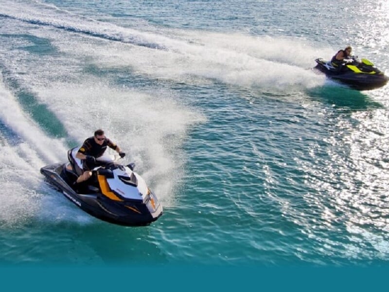 Deux jetskis noirs et jaunes glissant sur une mer calme avec des traces blanches d'écume derrière eux.