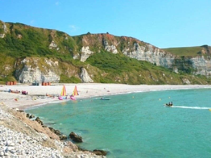 Plage avec des falaises blanches, des parasols colorés et des baigneurs au bord de l'eau turquoise.