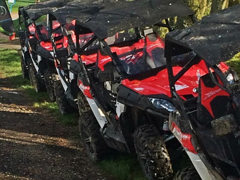 Rangée de quads rouges stationnés sur un terrain herbeux avec des ombres d'arbres au-dessus.