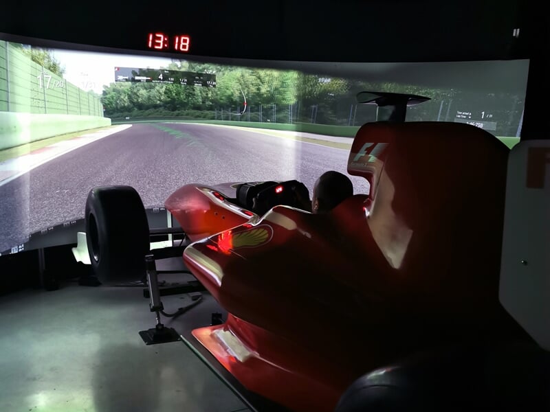 Simulateur de conduite automobile avec vue immersive sur circuit, voiture rouge en premier plan dans une salle sombre.