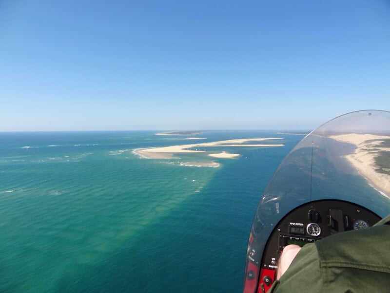 Vue aérienne depuis un ULM survolant une côte avec des plages de sable blanc et une mer turquoise.