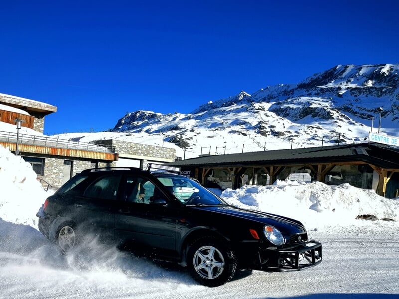 Subaru noire dérapant sur la neige lors d'un stage de pilotage rallye sur circuit glace à l'Alpe d'Huez en montagne.