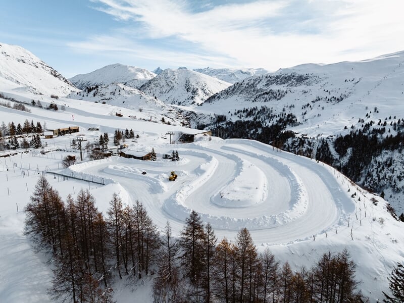 Vue aérienne d'un circuit de glace enneigé en montagne avec des pistes sinueuses entourées de sapins et de sommets