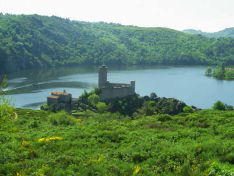 Château fort entouré d'eau et de collines verdoyantes sous un ciel clair, paysage naturel paisible.