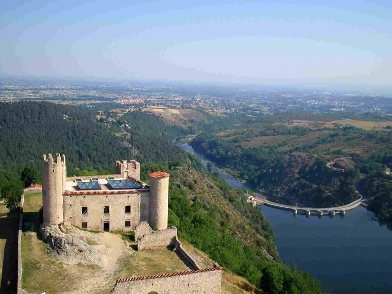 Château médiéval perché sur une colline avec une rivière sinueuse et un paysage vallonné en arrière-plan.