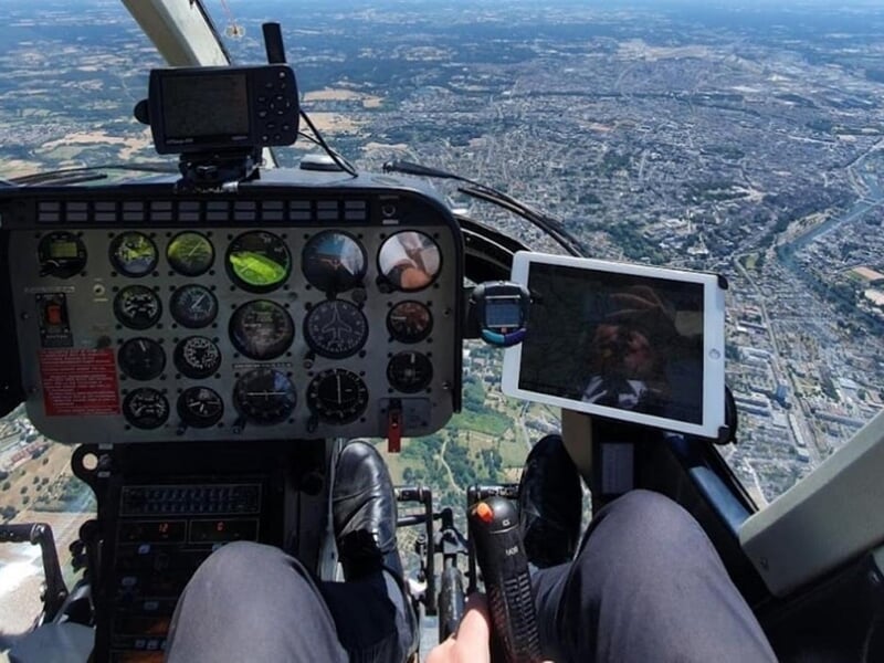 Vue depuis l'intérieur d'un hélicoptère en vol, montrant le tableau de bord et la ville en contrebas.