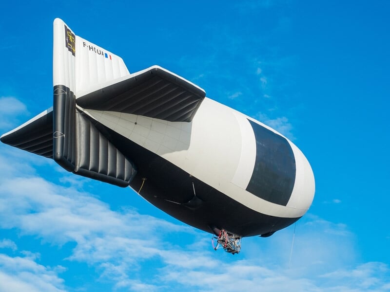 Dirigeable noir et blanc volant dans un ciel bleu clair avec quelques nuages, vu de côté.