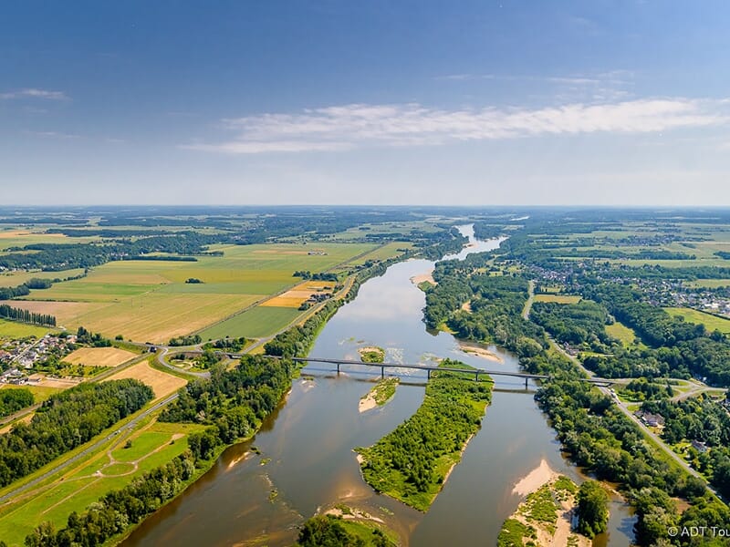 Vue aérienne d’un fleuve traversant une campagne verdoyante avec un pont au centre.
