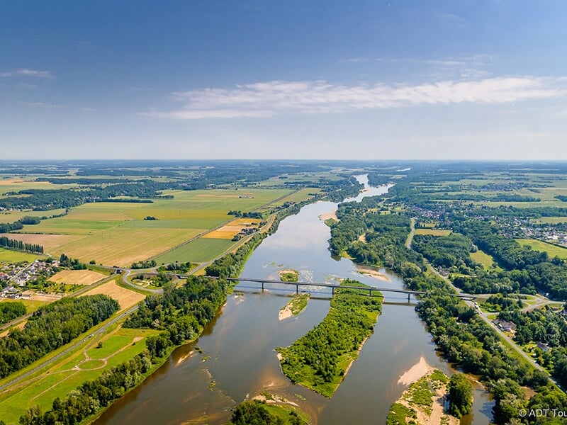 Vue aérienne d’un fleuve traversant une campagne verdoyante avec un pont au centre.