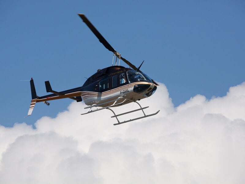 Hélicoptère noir et blanc en vol dans un ciel bleu avec des nuages blancs en arrière-plan.