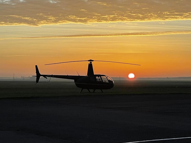 Hélicoptère silhouetté au lever du soleil sur un terrain dégagé.
