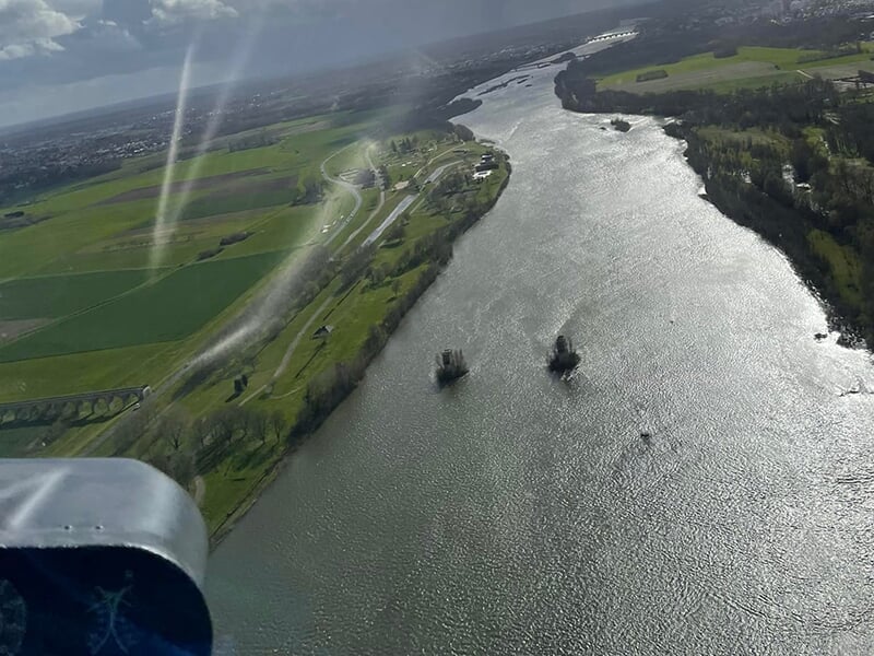 Vue aérienne d'une rivière sinueuse bordée de champs verts et d'infrastructures rurales.