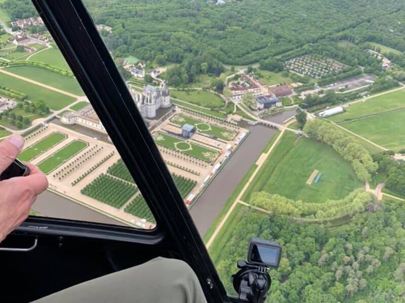 Vue aérienne d'un château entouré de jardins symétriques et d'un canal, prise depuis l'intérieur d'un hélicoptère.