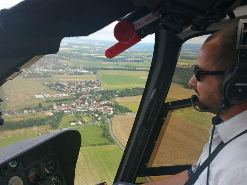 Pilote portant un casque Bose et des lunettes de soleil, survolant un paysage verdoyant avec une infrastructure au sol.