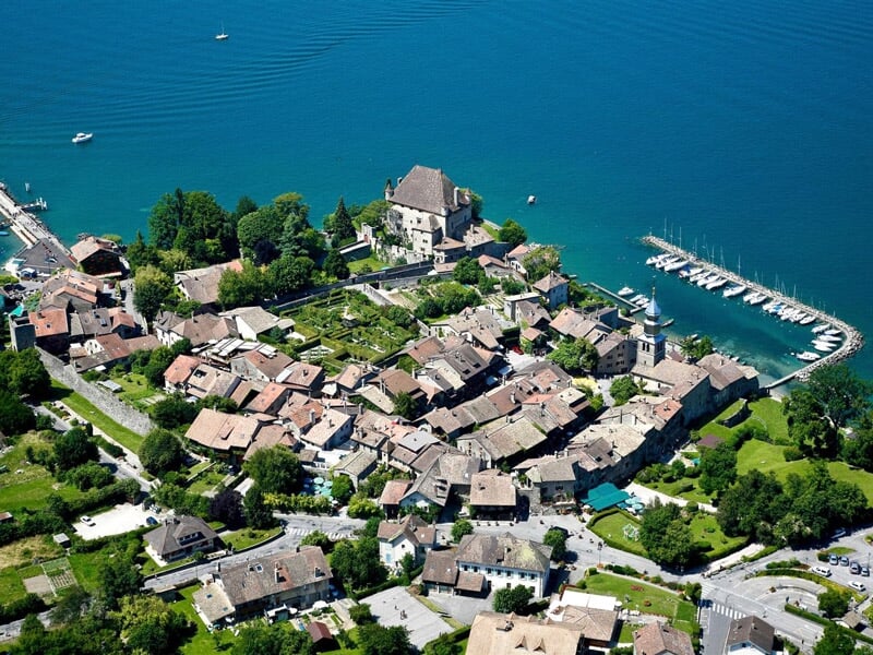 Vue aérienne d'un village au bord d'un lac avec des maisons, des arbres et un port de plaisance.