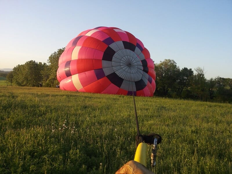 Montgolfière colorée au sol, partiellement dégonflée dans une prairie, capturée au coucher du soleil