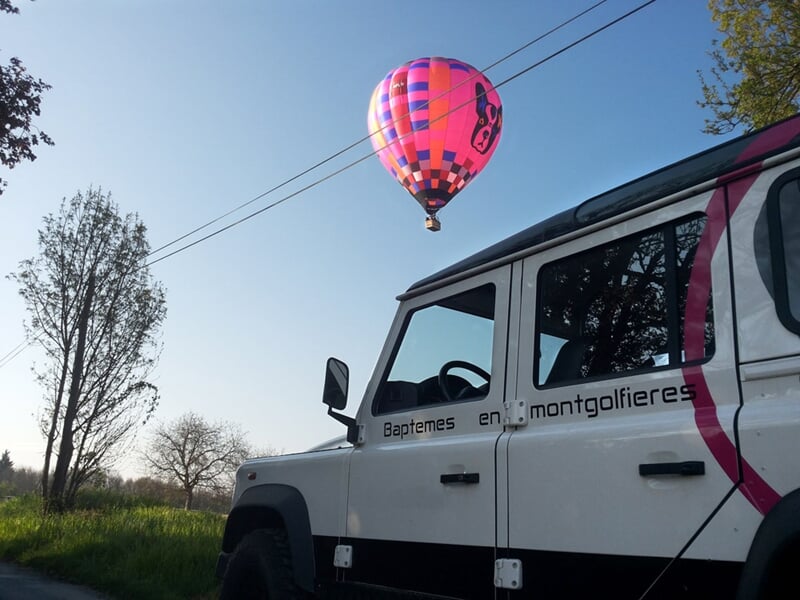Montgolfière rose et violette dans le ciel, survolant un véhicule tout-terrain marqué