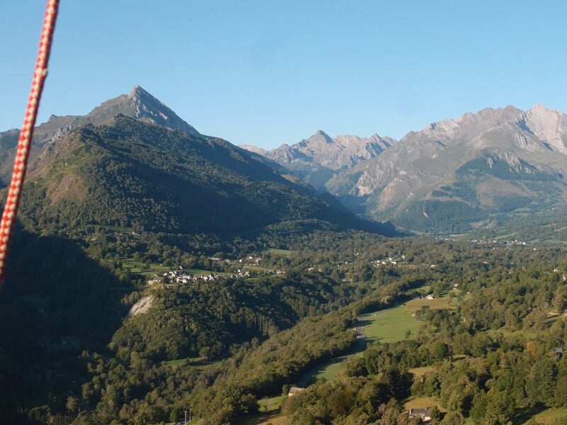 Vue panoramique sur une vallée verdoyante des Pyrénées, avec des montagnes escarpées et un ciel bleu clair