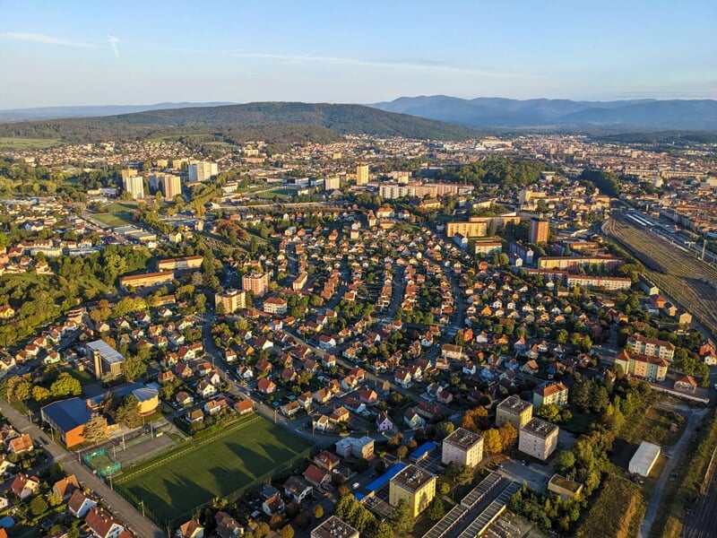 Vue aérienne d'une ville au coucher du soleil avec des bâtiments, des arbres et des montagnes à l'horizon